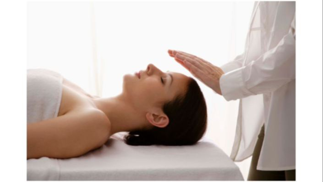 Reiki treatment woman on table and practitioner's hands overing over her head