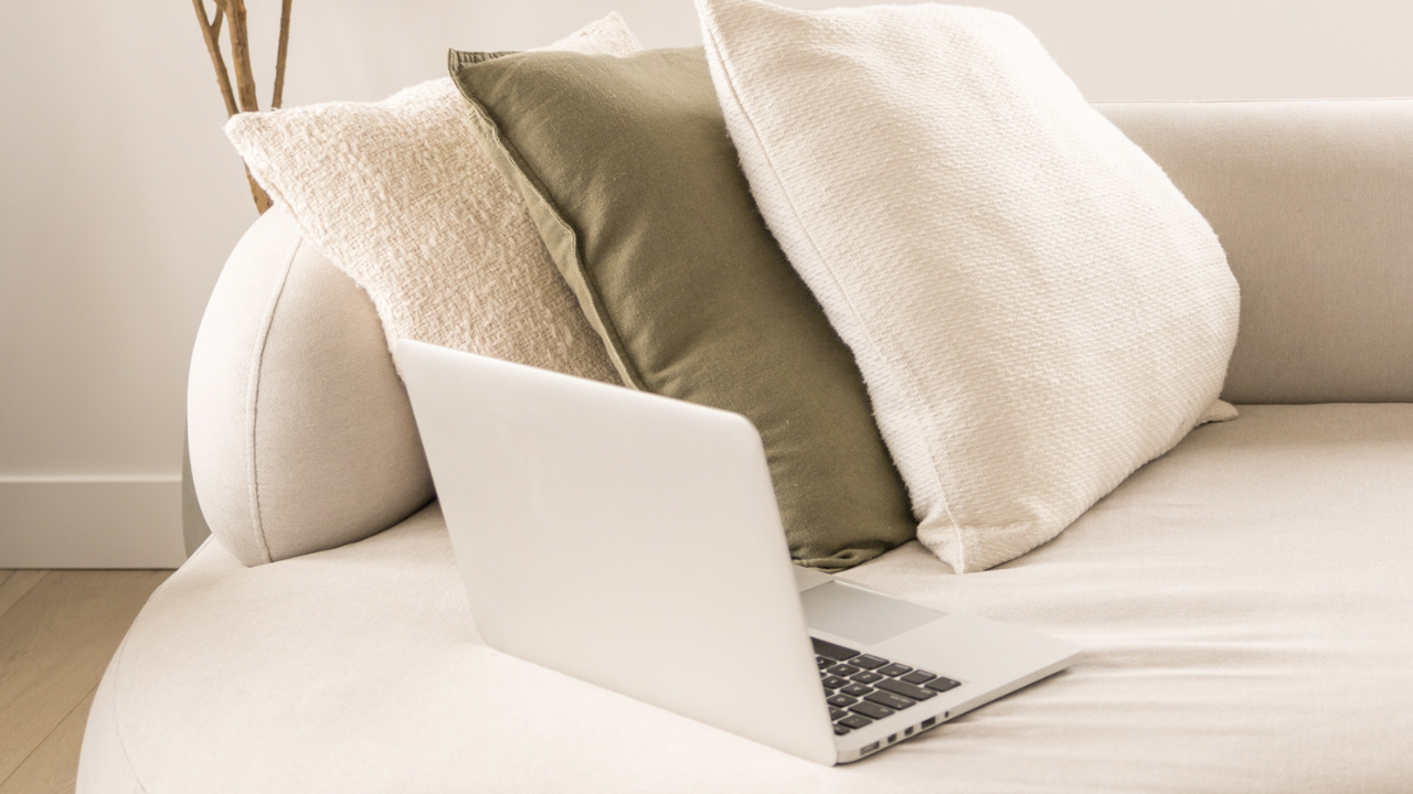A laptop resting on a sofa with neutral cushions, representing the creative workspace of a female leader building her business through storytelling.