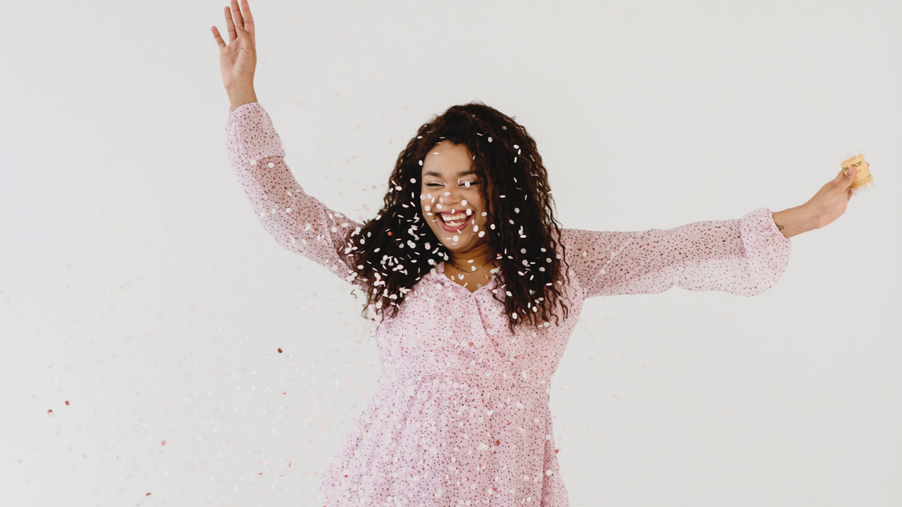Happy female entrepreneur throwing confetti to celebrate business success and joy as a frequency for magnetic client attraction and neurobiology-backed growth.