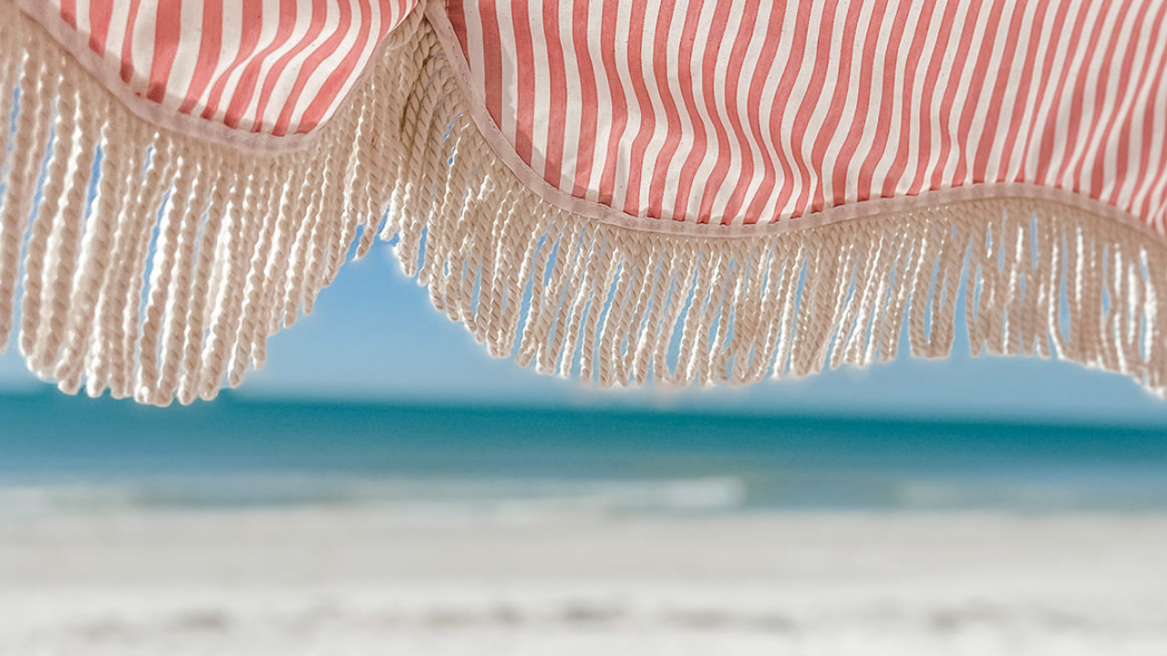 Striped beach parasol with fringe overlooking the sea, evoking calm, joy and relaxed summer energy