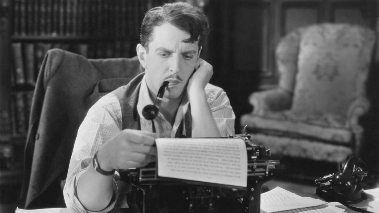 A male writer with furrowed eyebrows, reading his manuscript still in the typewriter