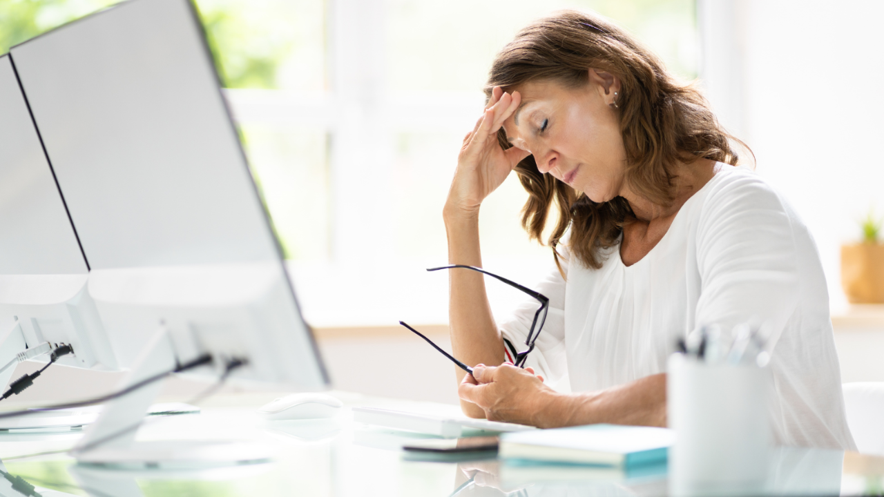 A woman massaging her temple out of stress in front of her computer screen.