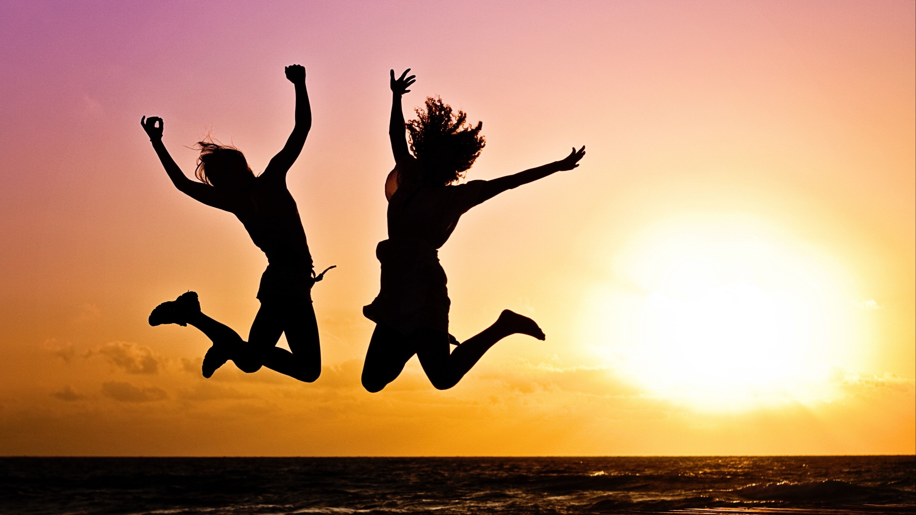 Two people looking very happy jumping on a beautiful sunset