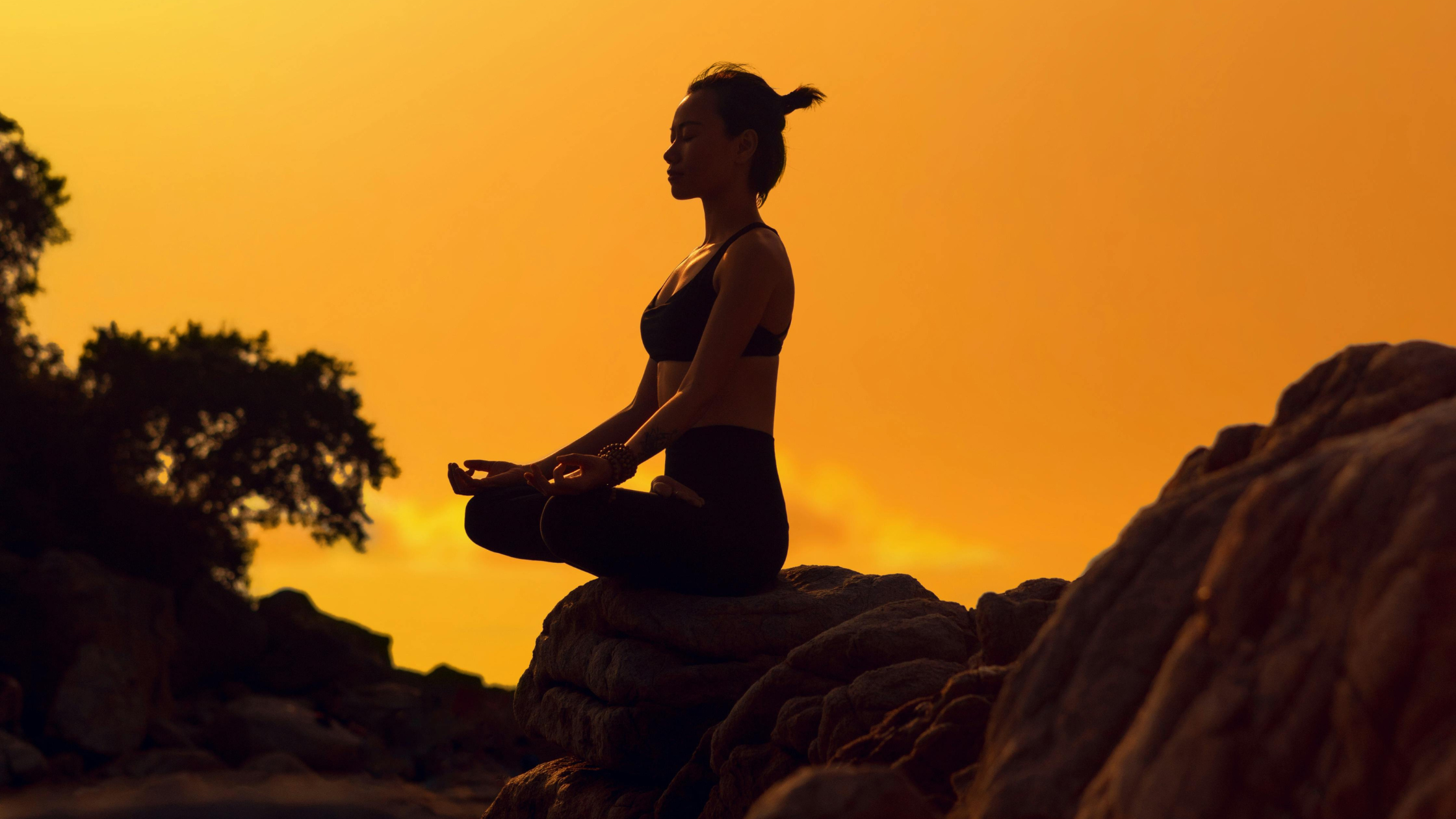 woman meditating in lotus position on rocks at sunset