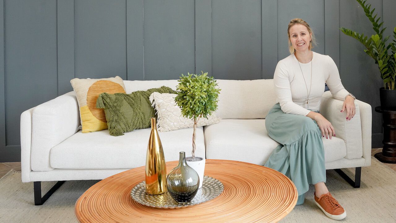 Photo of a blonde white woman, Brazilian-American home stager sitting on a cream sofa in a beautifully staged living room at the Staging Studio Master Class