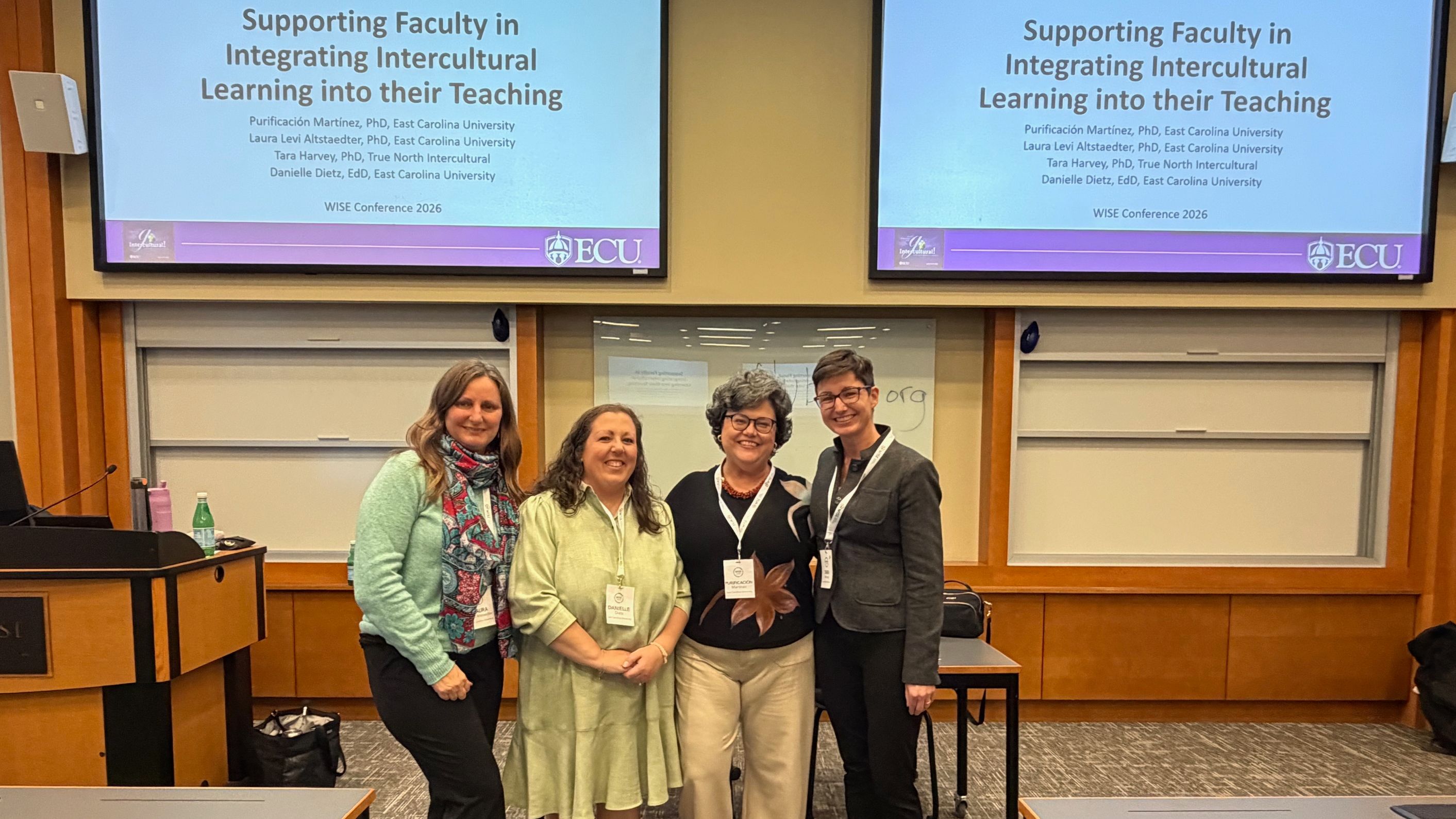 Four women stand together in front of screen that reads 