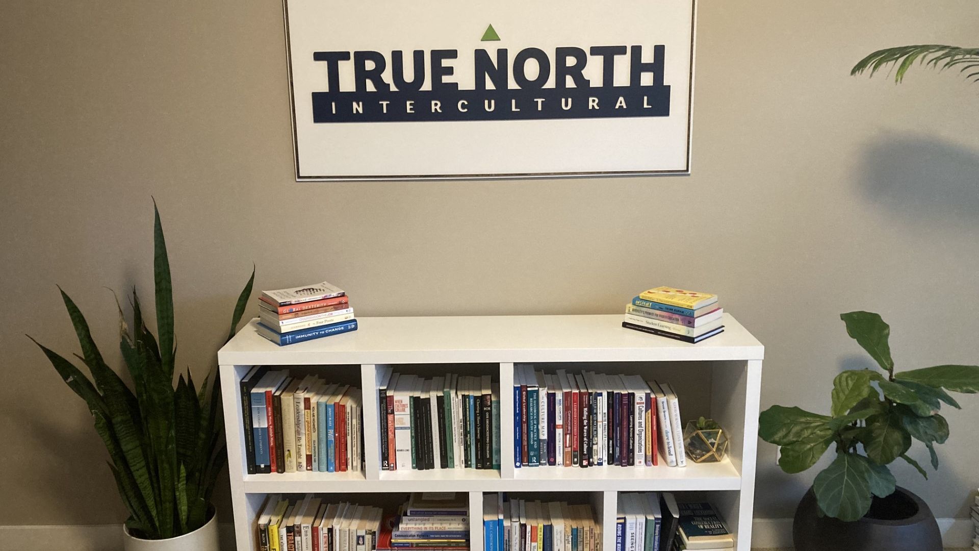 Book shelf, plants, and True North Intercultural sign