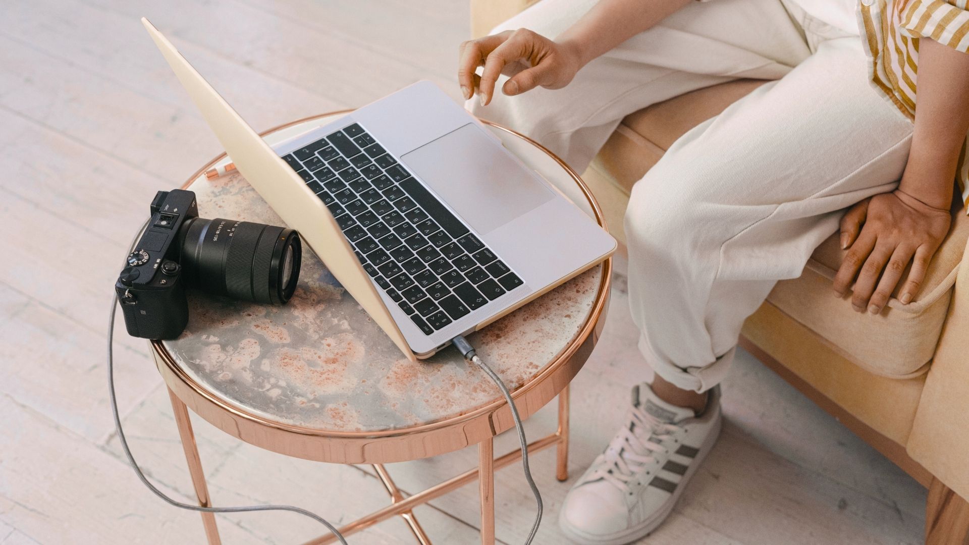 Person working on a laptop beside a camera, representing online photography and Photoshop education.