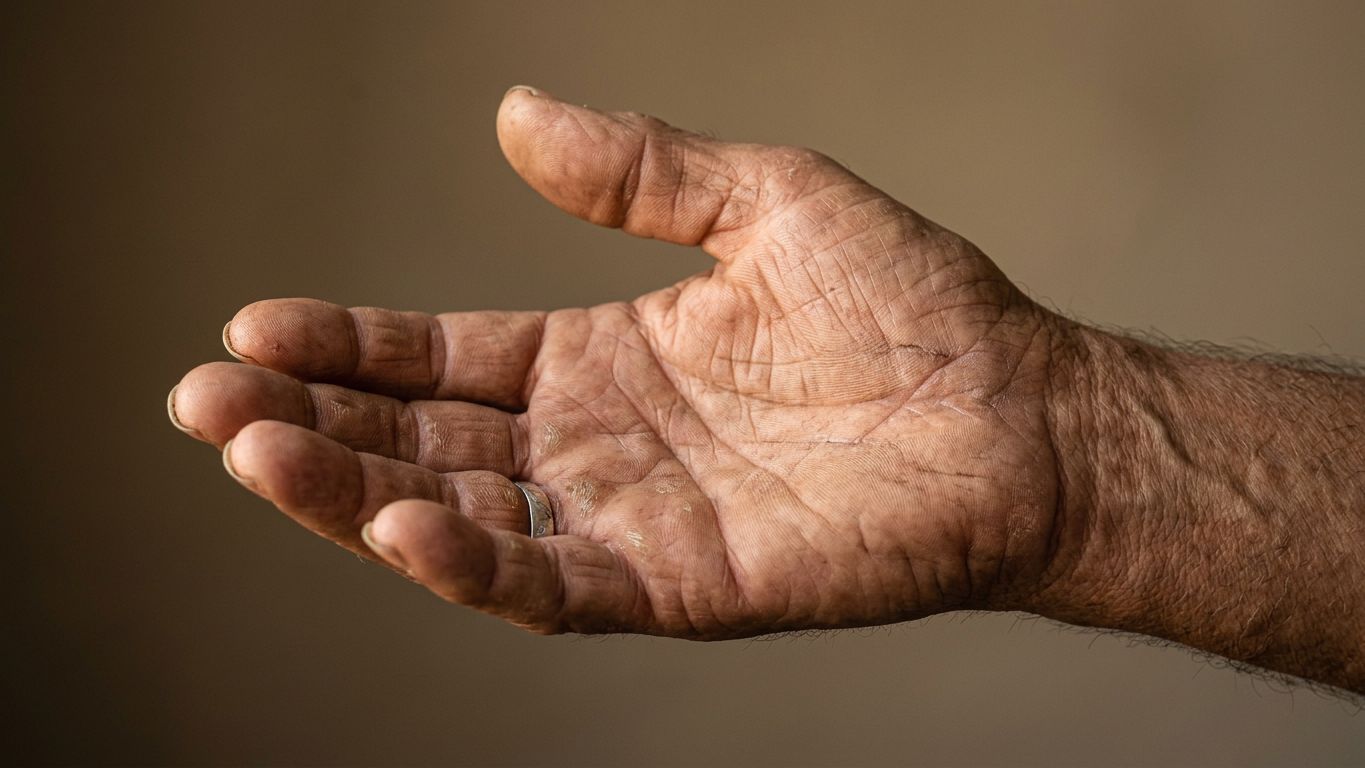 Mano experimentada y abierta extendida hacia arriba con luz lateral cálida sobre fondo neutro cálido