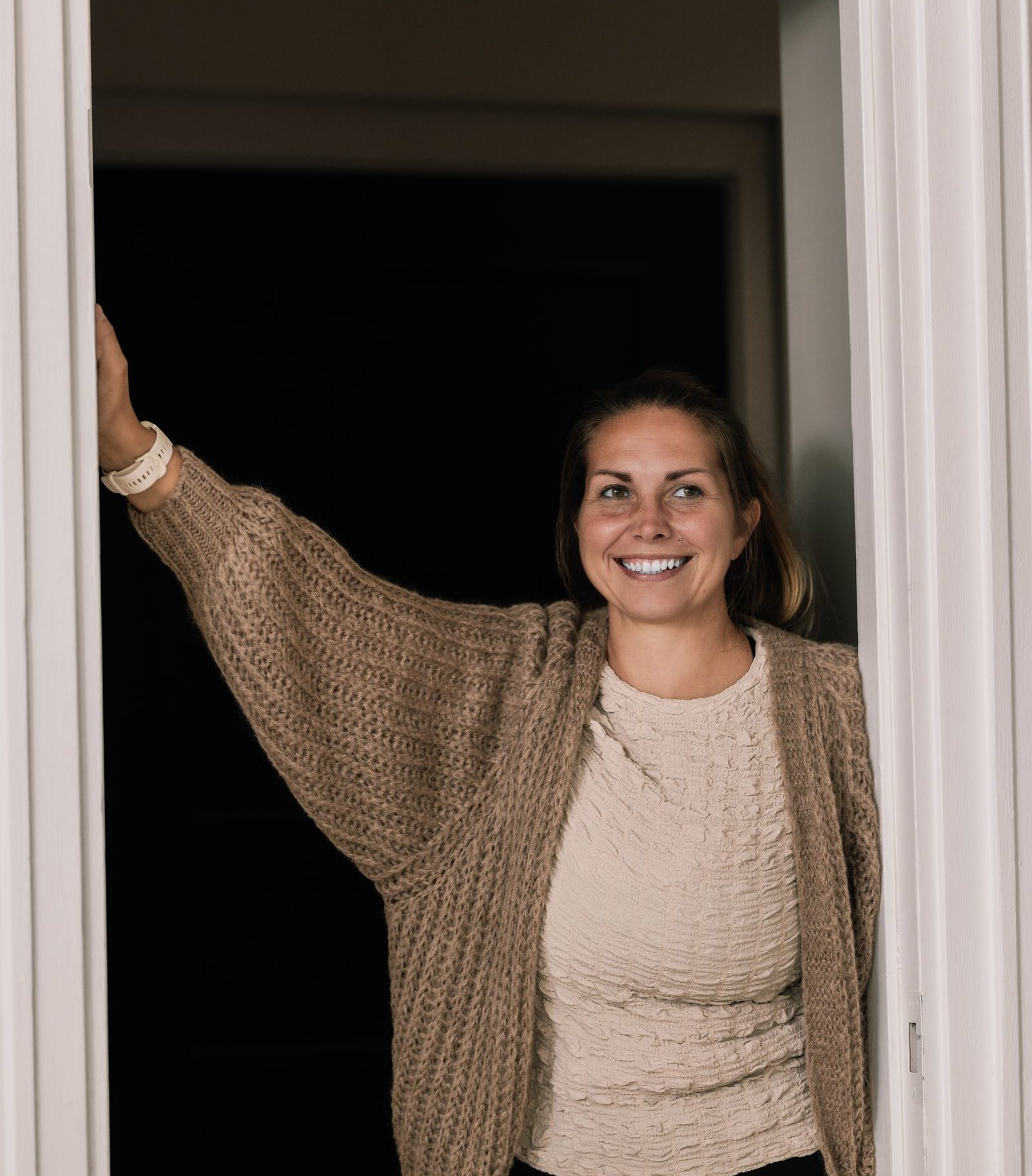 Therese Øyane i døråpningen, smilende i strikkejakke