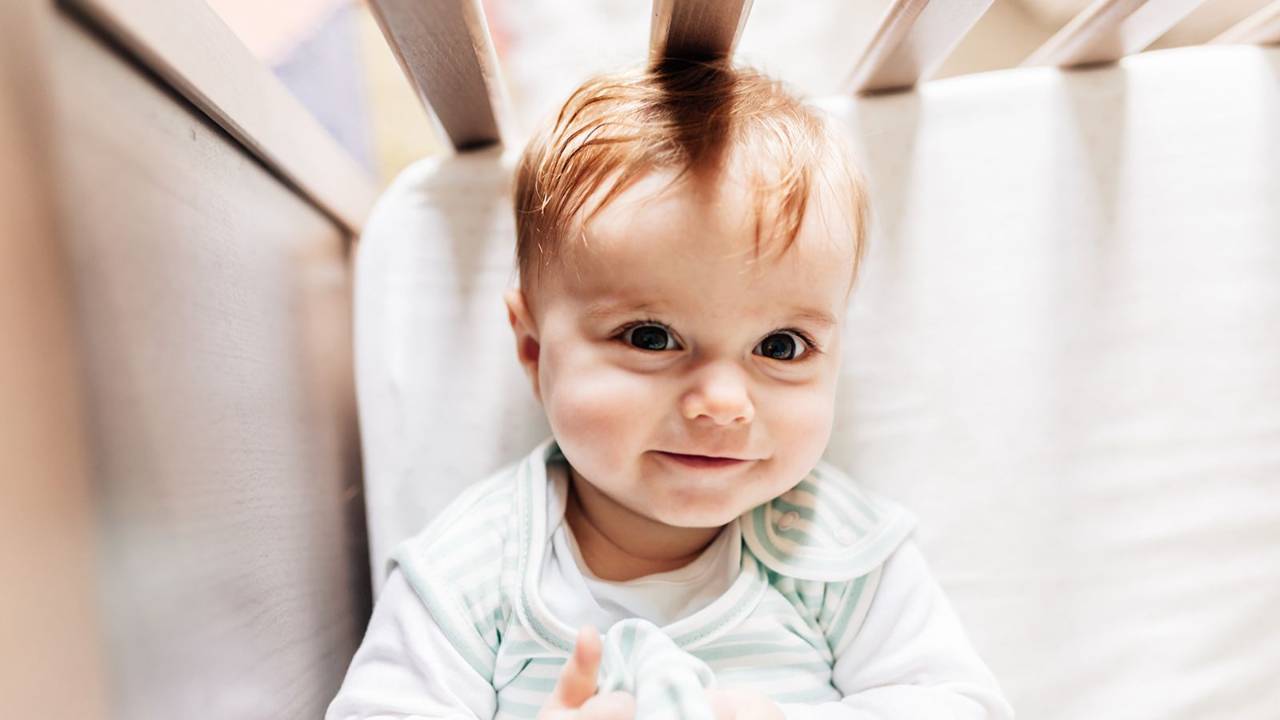 A six month old baby awake and happy in their crib.