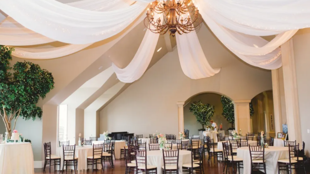 Elegant LDS wedding reception venue featuring flowing white ceiling draping, chandeliers, round guest tables, and a beautifully decorated ballroom designed for a timeless and romantic wedding celebration.