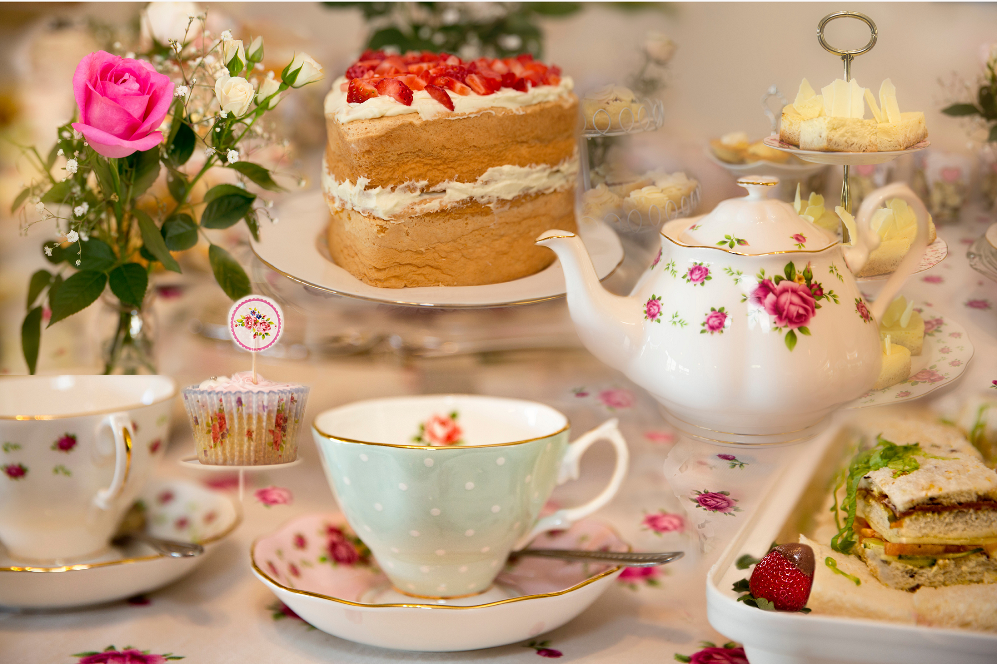 Elegant bridal shower tea party featuring floral china, a strawberry cake, tea cups, finger sandwiches, and dessert trays arranged on a beautifully decorated table for a bride-to-be celebration.