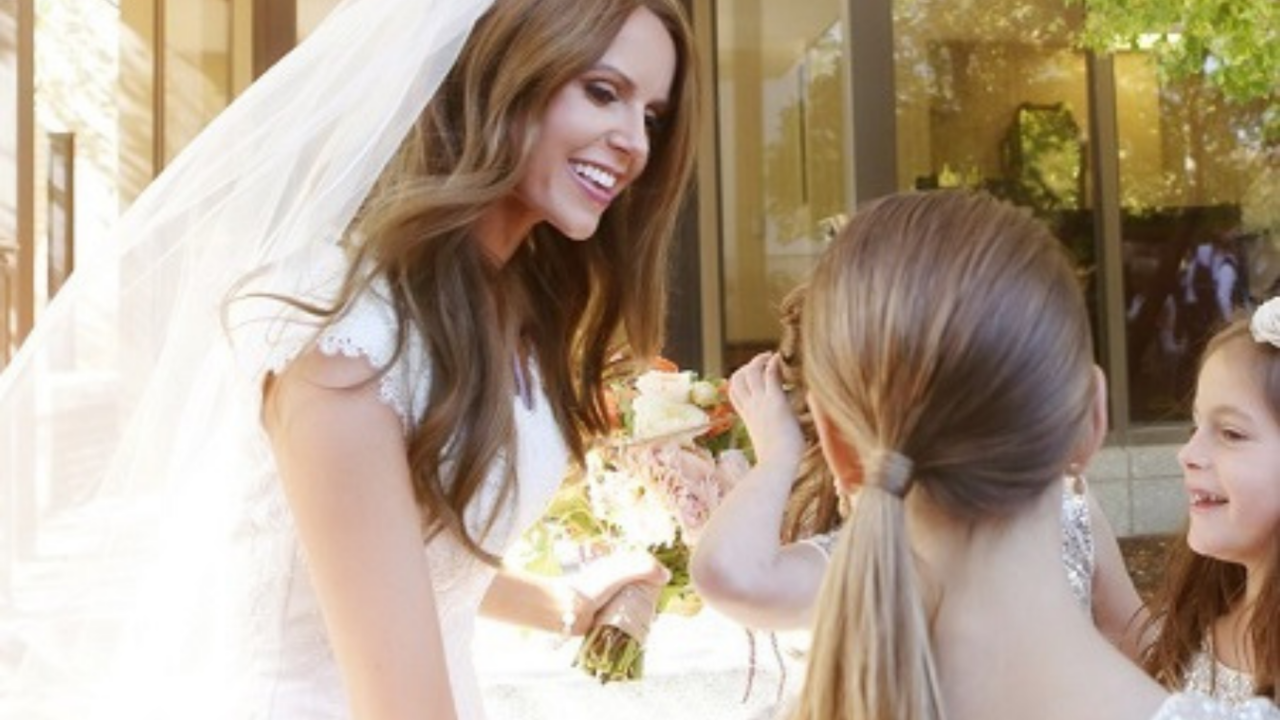 Smiling LDS bride in a modest wedding dress and veil talking with young flower girls outside the temple after her wedding ceremony in warm golden sunlight