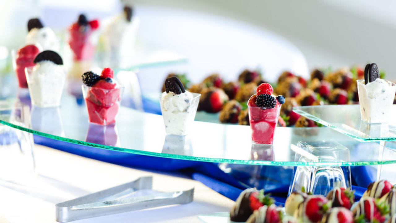 Elegant wedding dessert display featuring miniature parfaits, fresh berries, chocolate-dipped strawberries, and individual sweet treats arranged on modern glass serving trays, showcasing creative reception dessert options for wedding guests.