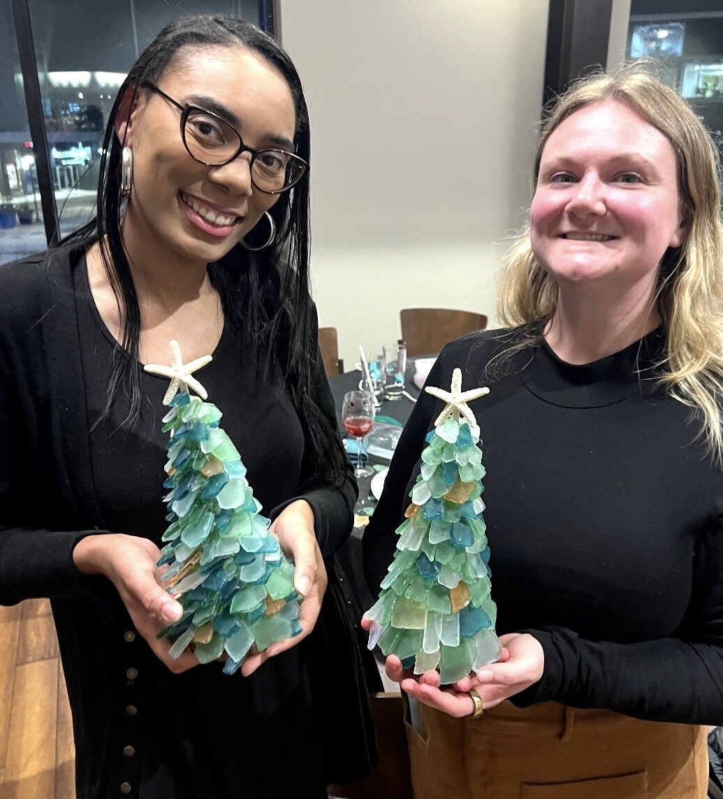 Two guests holding blue and green sea glass trees they made at an Artist at Heart event in Cleveland