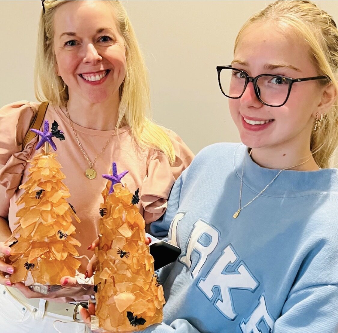 Two guests holding orange Halloween sea glass trees they made at Artist at Heart in Cleveland