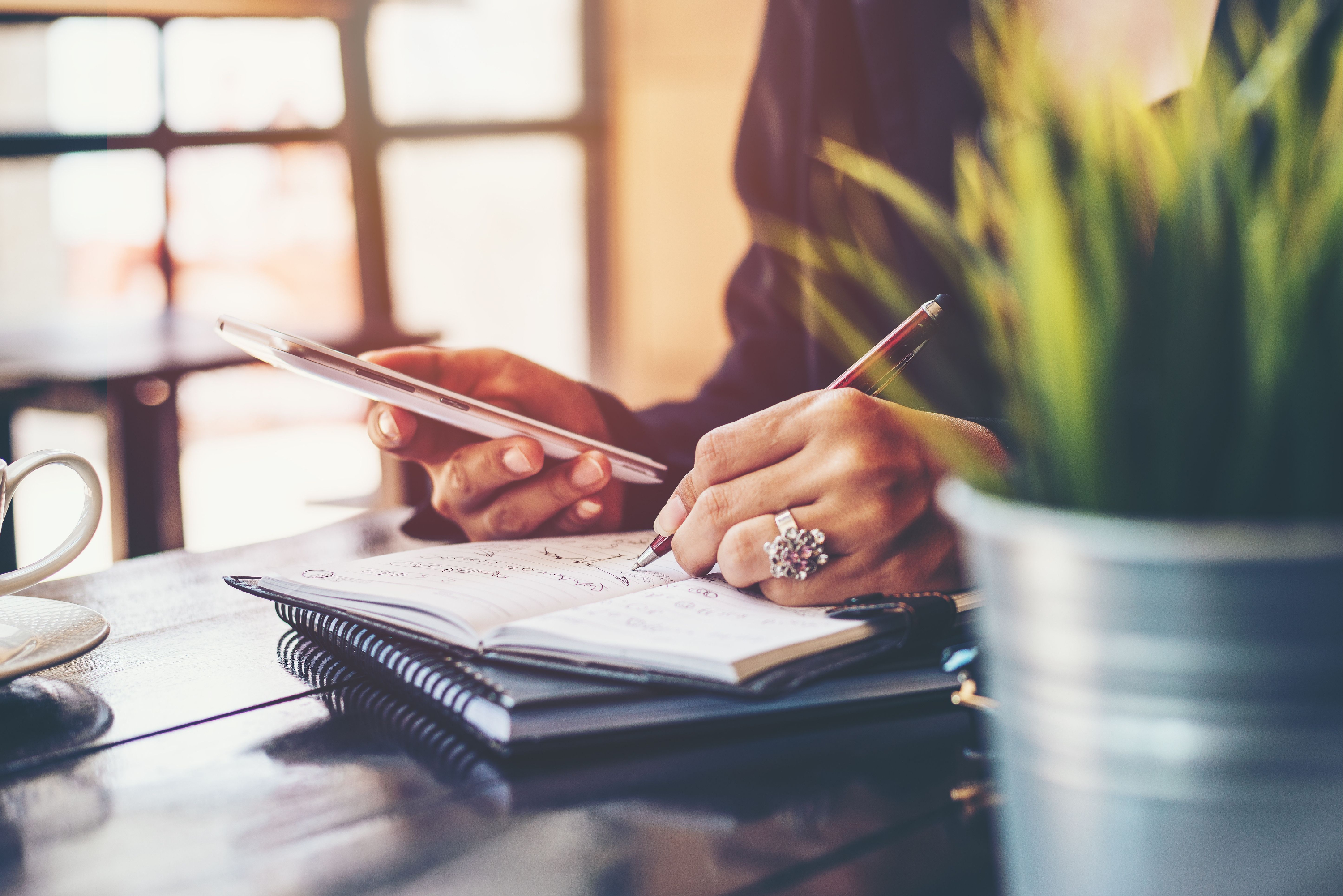 Hands writing planning notes in a notebook at a desk.