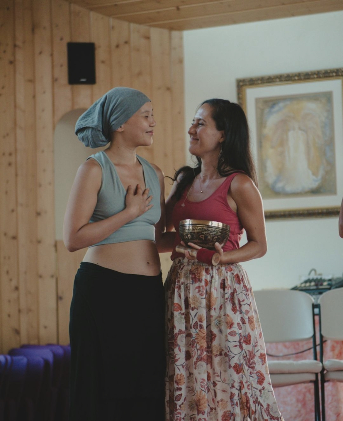 Leandra Rose holding a singing bowl, sharing a warm moment with a participant