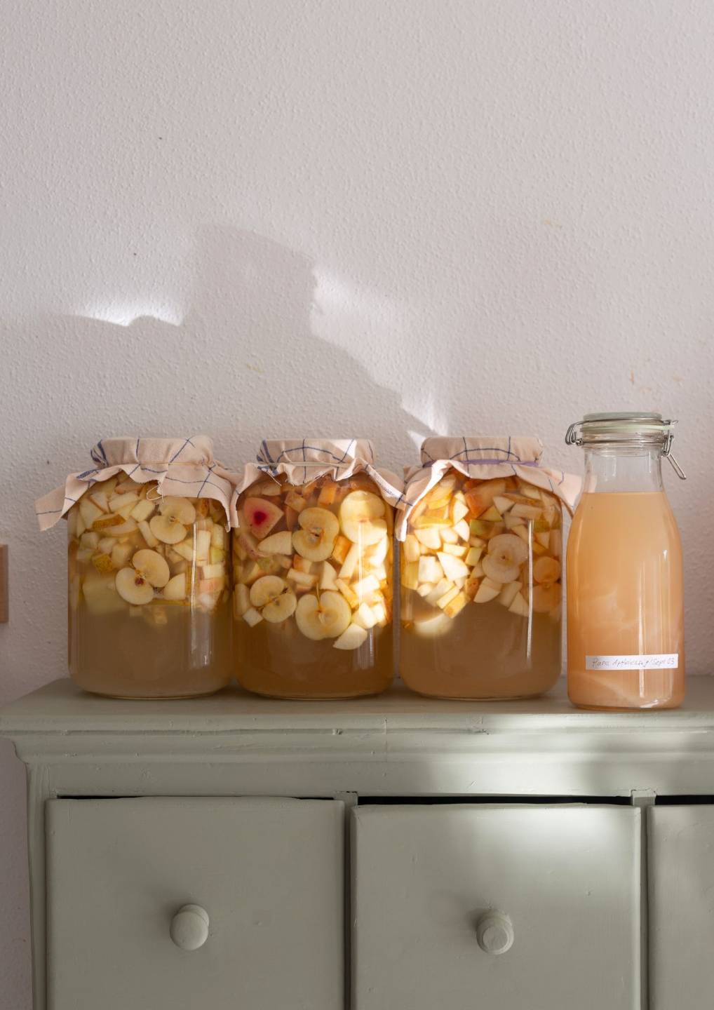 Gläser mit fermentierendem Apfel-Essig auf einer Kommode