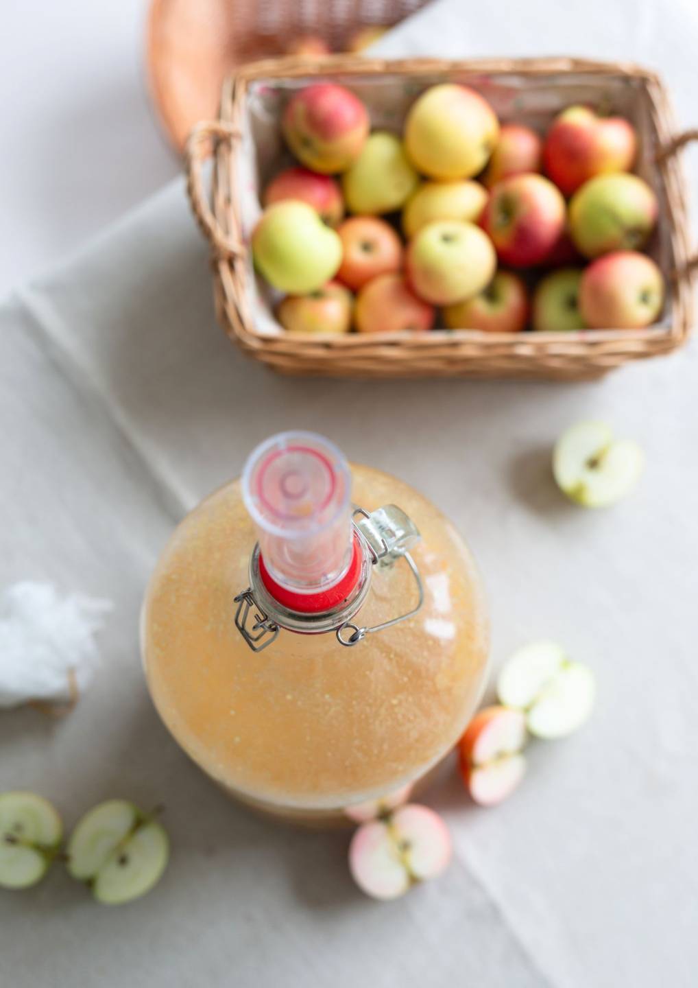 Korb frischer Äpfel neben Gärgefäß mit Gärröhrchen für Apfelessig