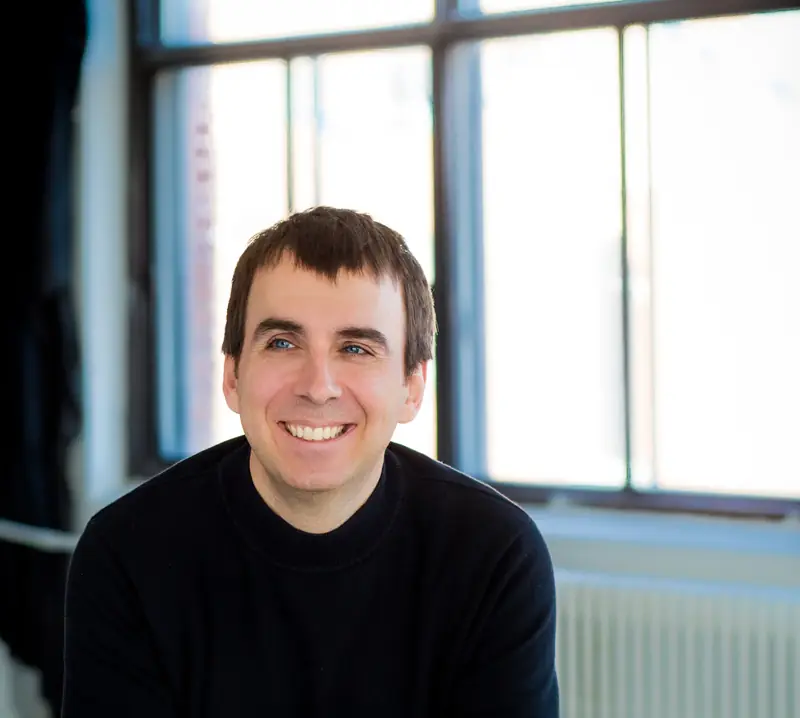 Philippe Bussière, souriant, assis devant une grande fenêtre d'atelier