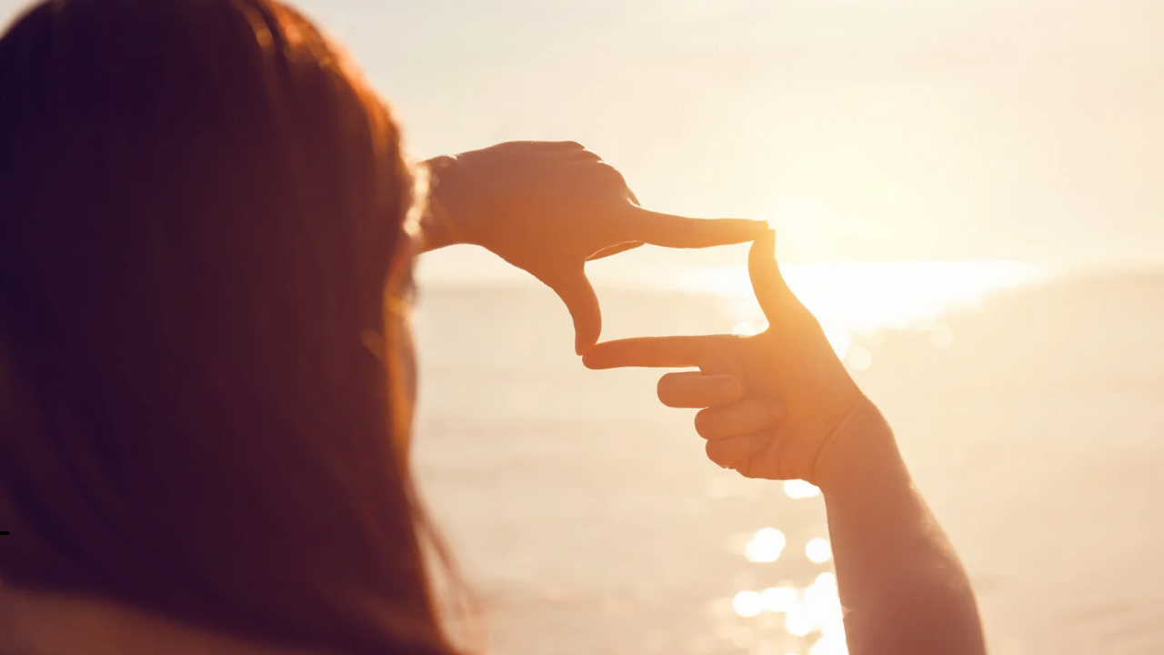 Woman looking through her fingers at the sunrise.
