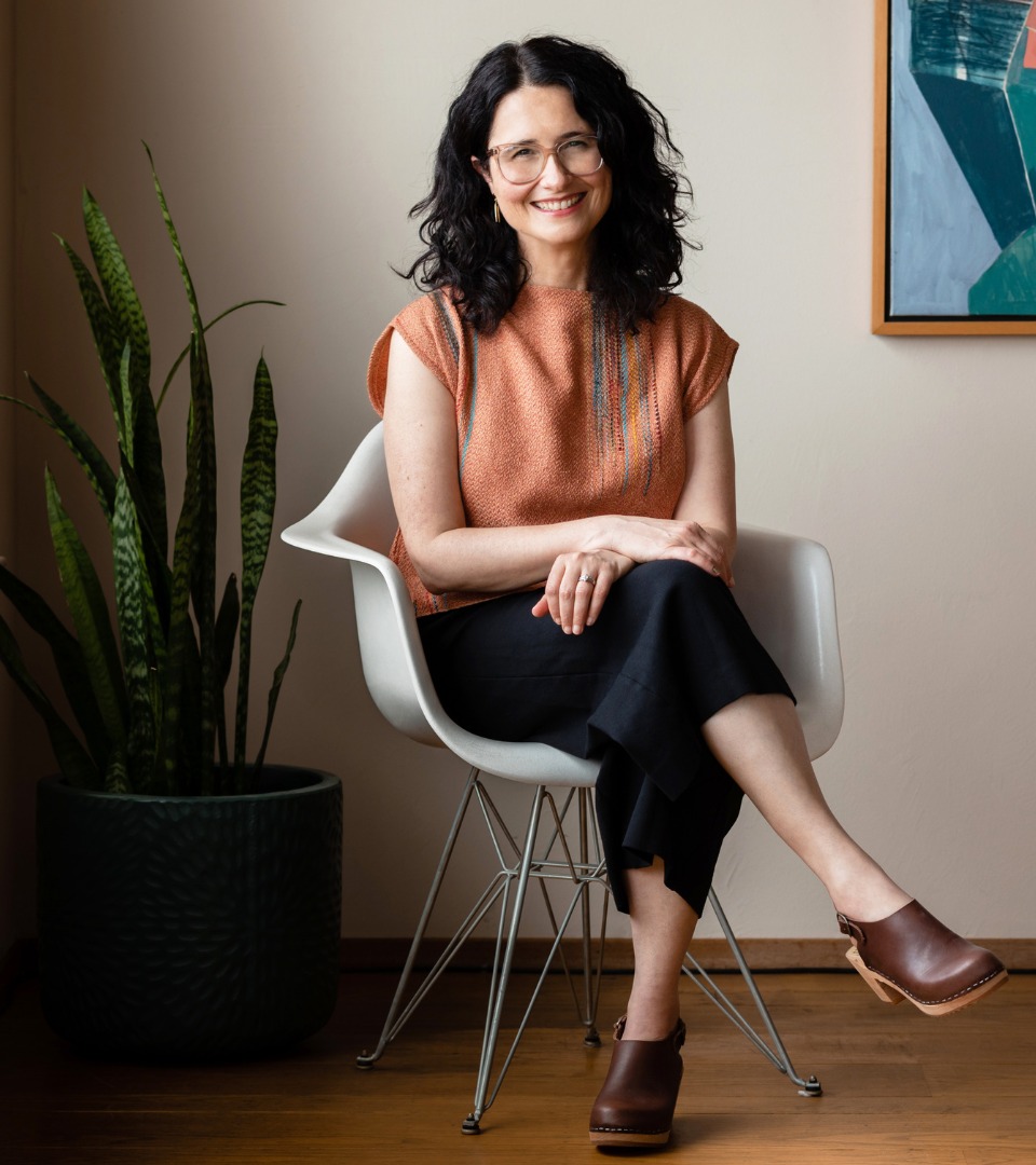 Lea Seigen Shinraku sitting in a white chair beside a plant, smiling