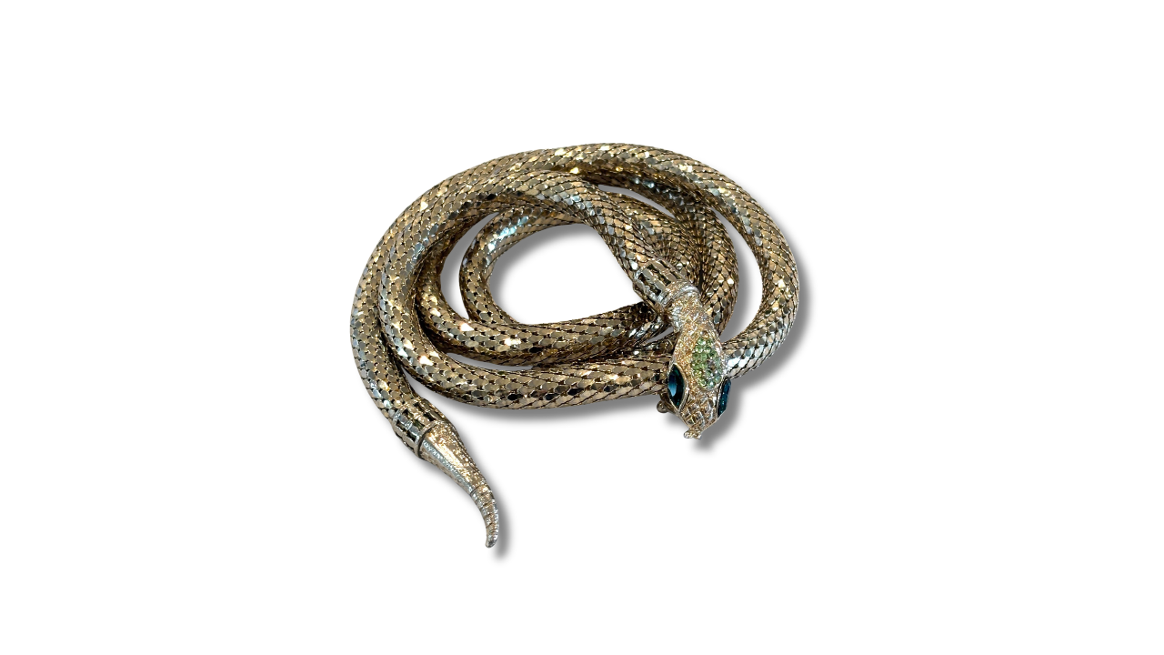A coiled silver snake-shaped object with a detailed textured pattern and a decorative blue-green eye, photographed against a white background.