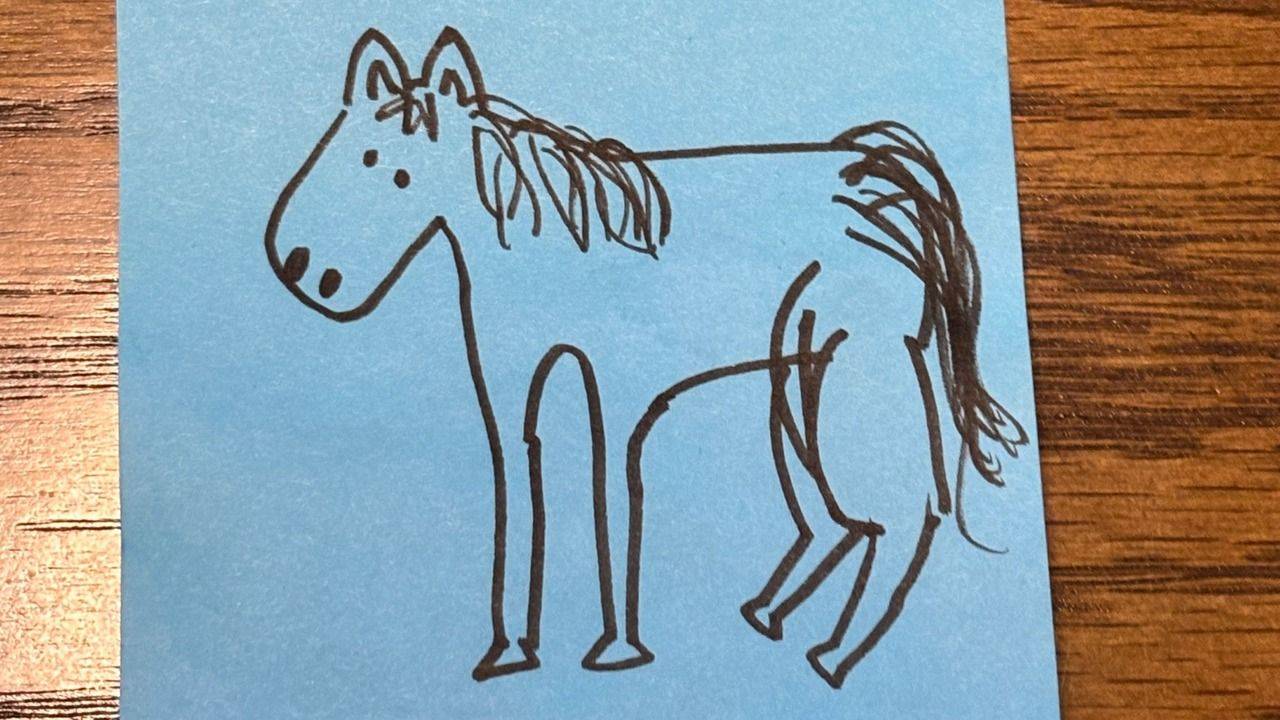 A hand-drawn horse on a blue post-it note on a wooden desk.