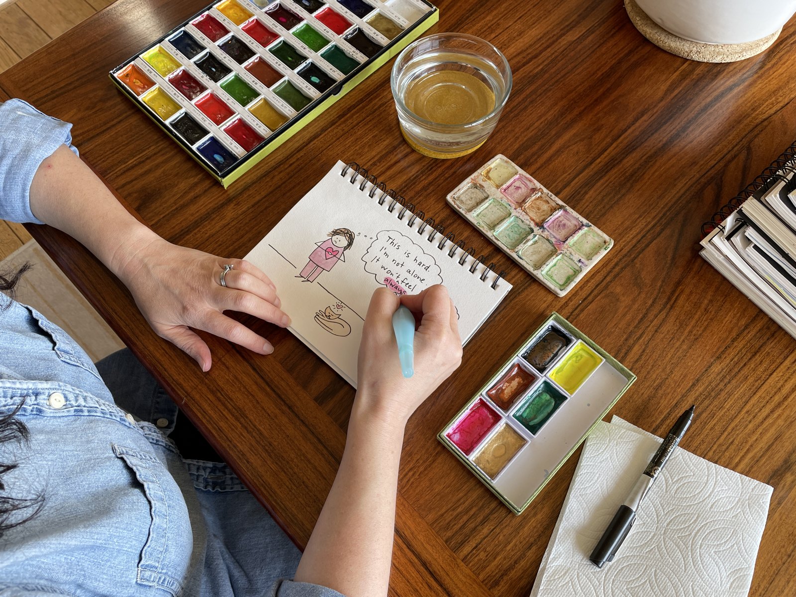 Lea art journaling at her table with watercolors and a journal page in progress