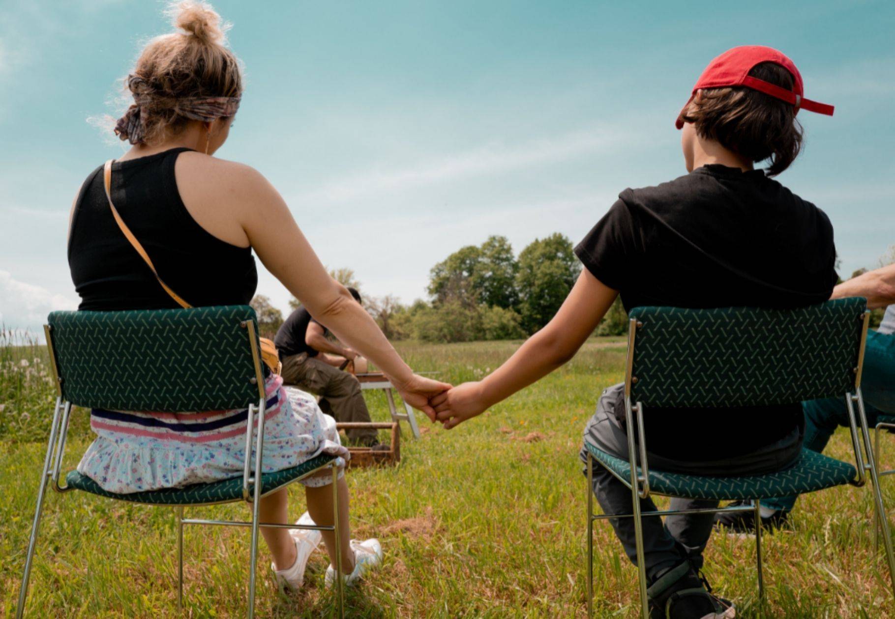 two tribal youth sitting in chairs in a field, connected by holding hands