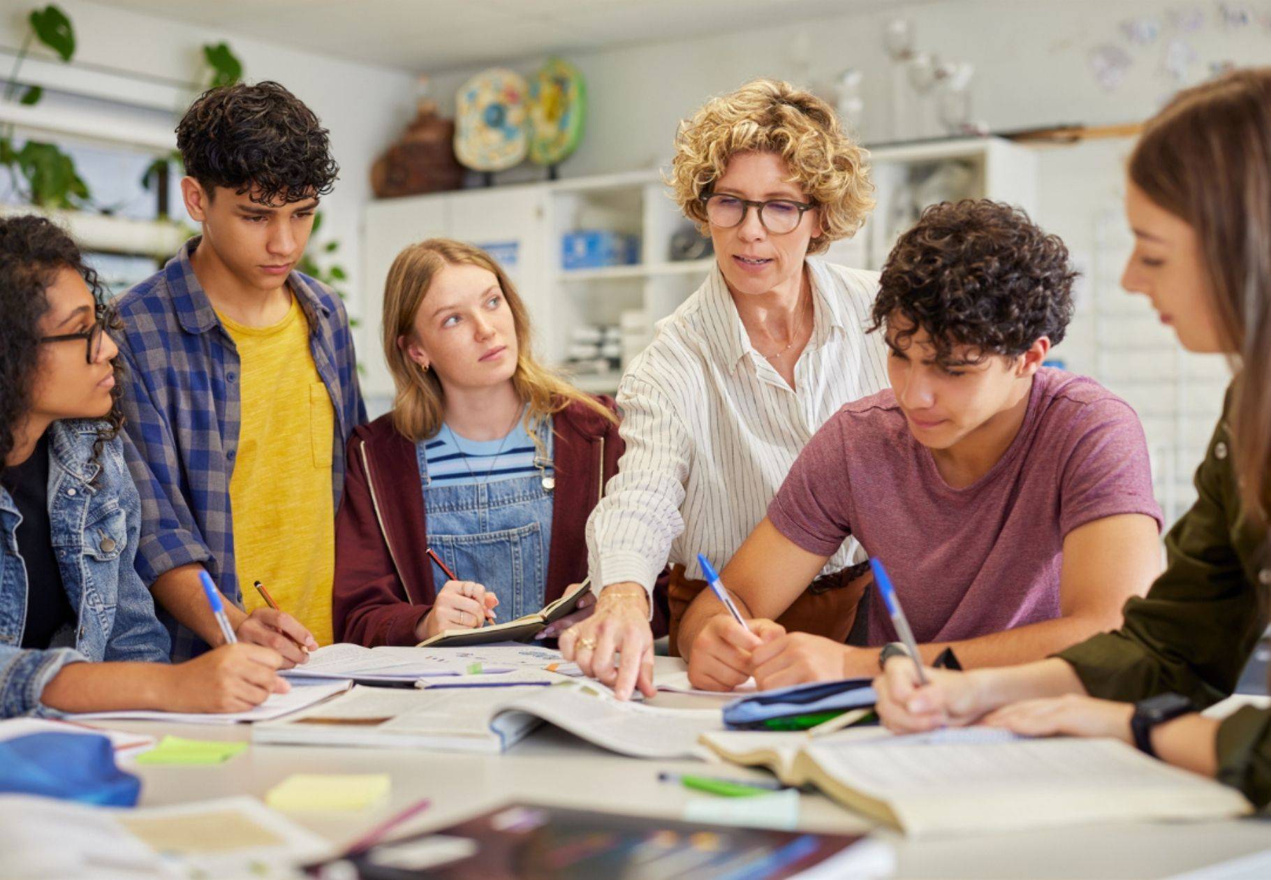 teacher instructing students with hand pointing to text on a desk
