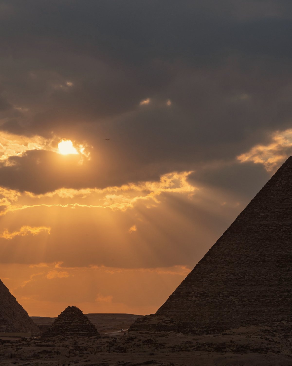 Sun breaking through clouds over the pyramids of Giza at dusk