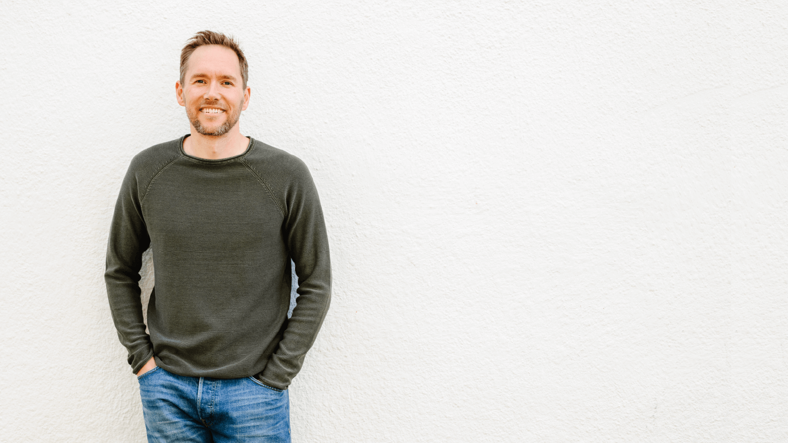 Picture of JD in green sweater leaning against a white wall