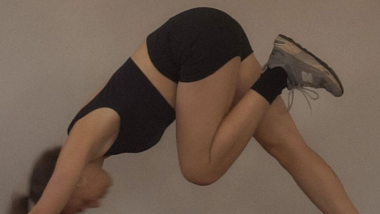 Person in black athletic wear bending forward against neutral wall