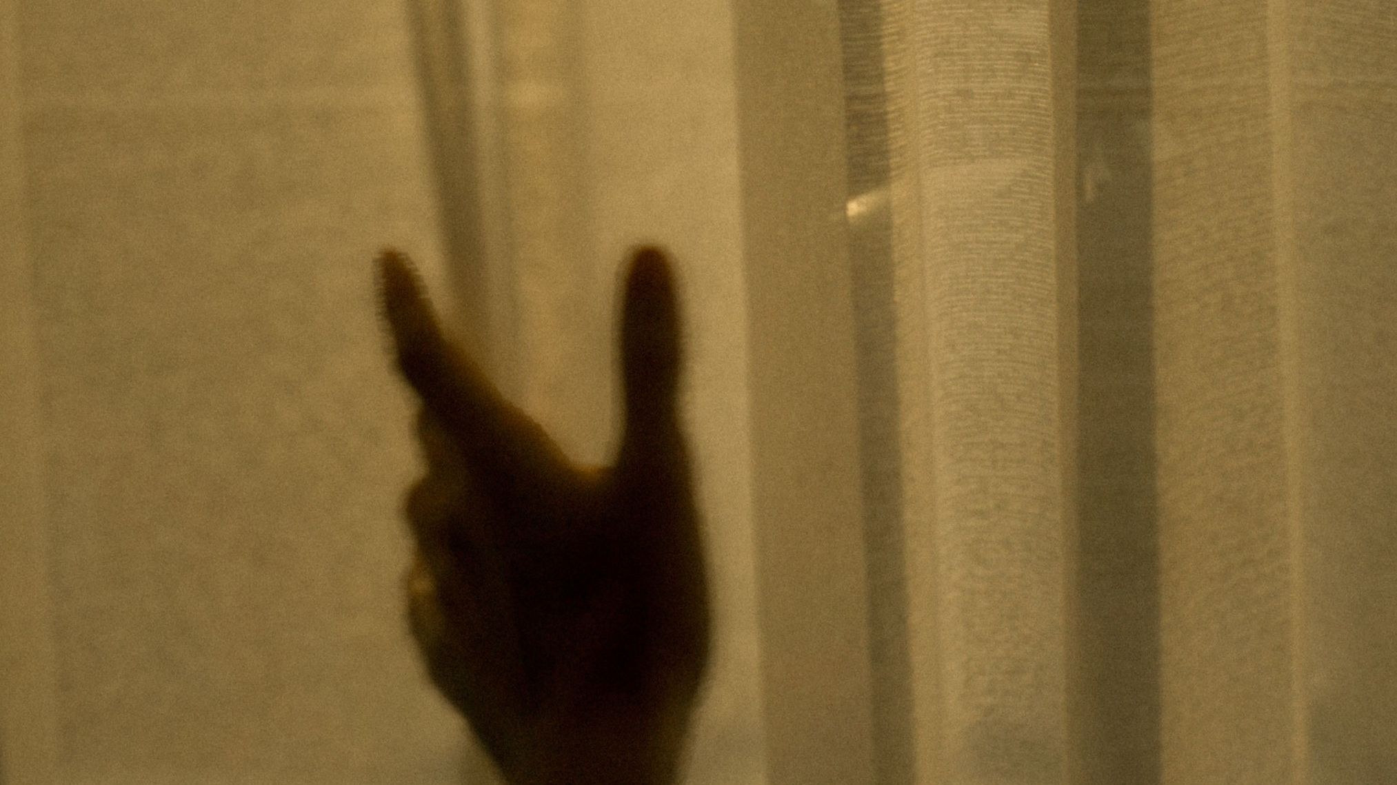 Hand reaching through sheer curtains toward warm light
