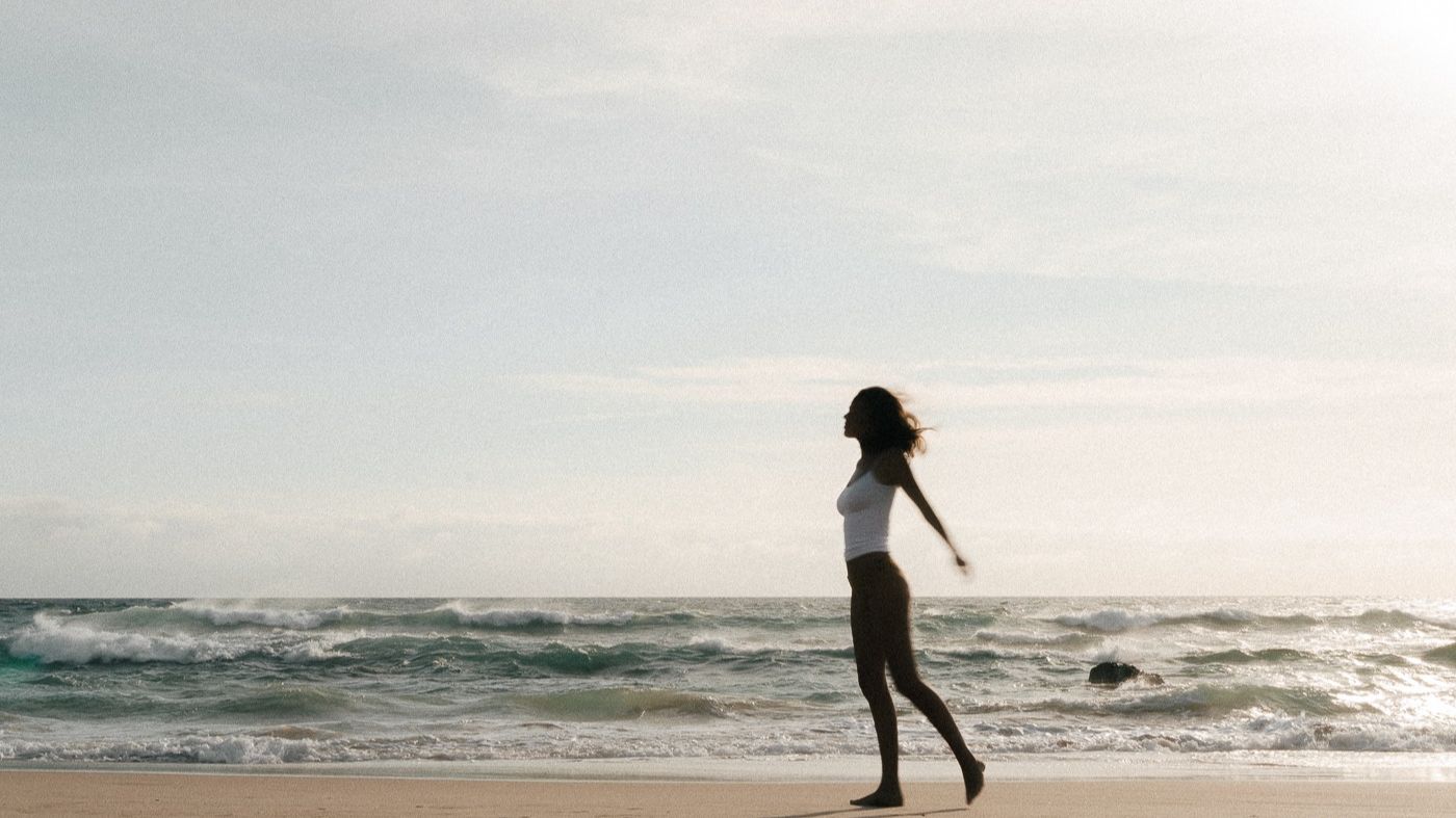 Woman jogging along sunny beach with waves in background