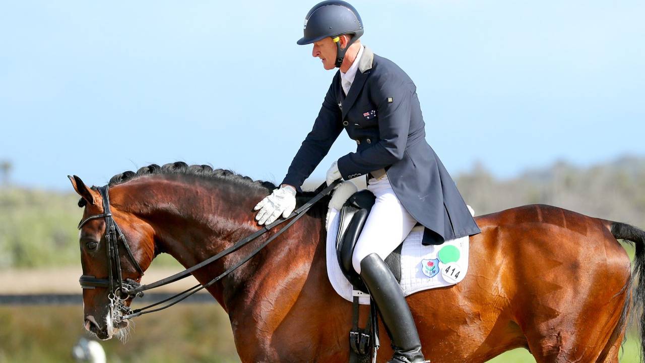 Brett Parbery pats a bay horse at the end of a dressage test, walking on a long rein.