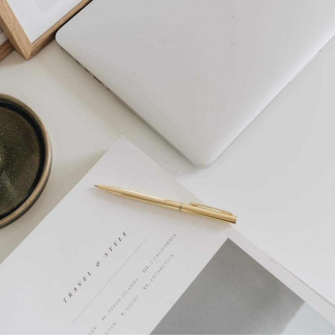 Close-up of a desk with a laptop, gold pen, and a magazine, symbolizing strategic planning and brand alignment.