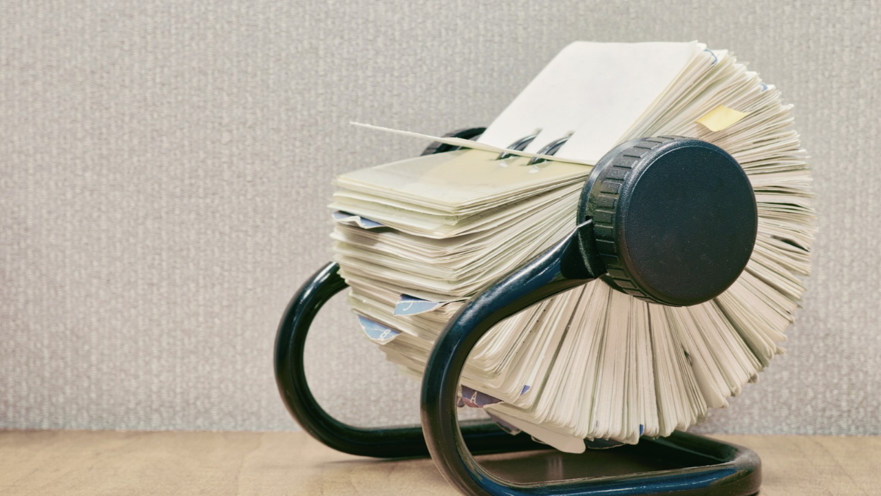Vintage Rolodex card file with fanned cards and alphabet tabs on a wooden desk.