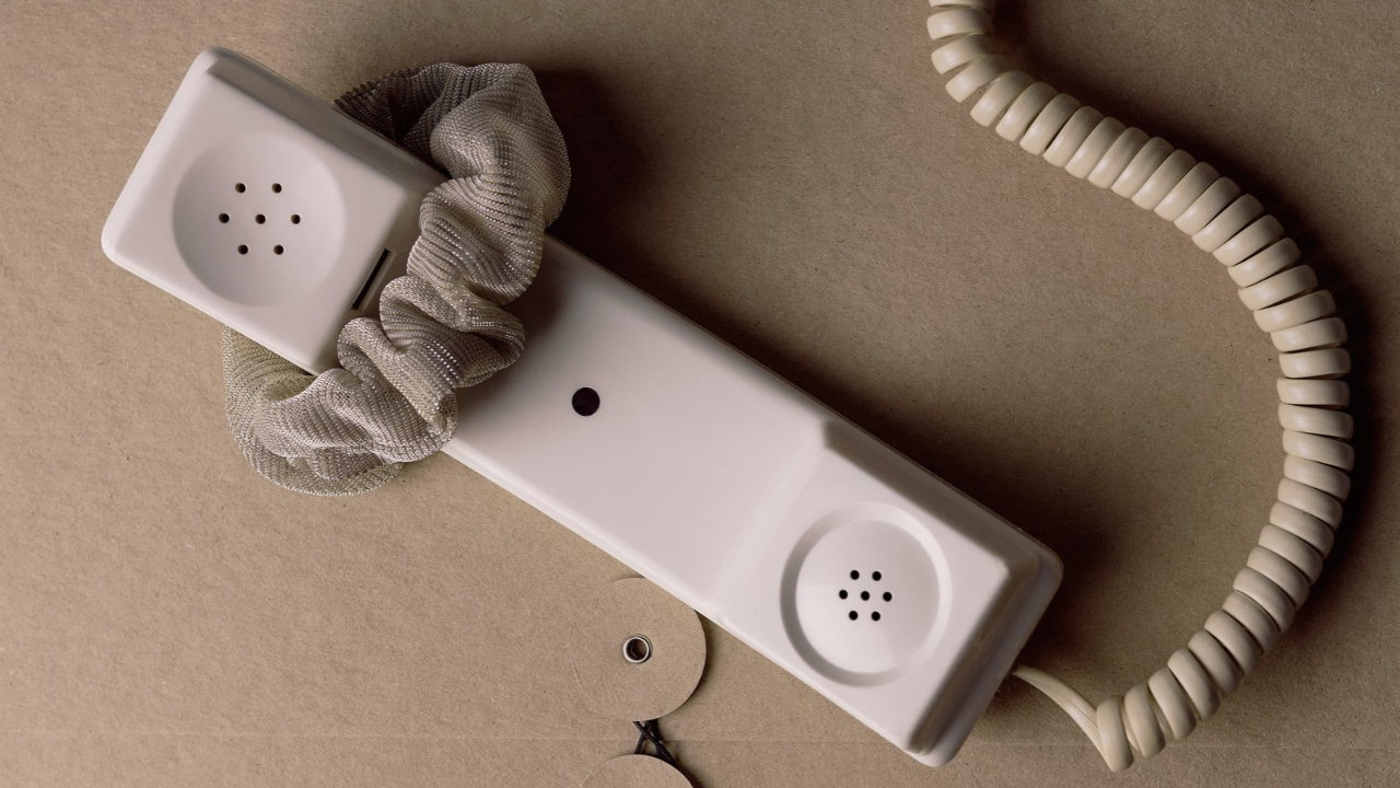 Cream rotary phone handset with a scrunchie on the cord, on a taupe background.