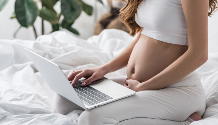pregnant mother sitting on a bed using computer