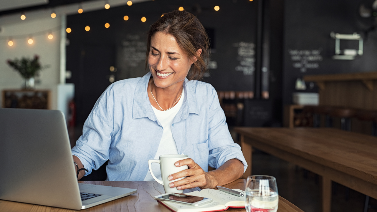 Woman with coffee on hand while looking happily in her laptop