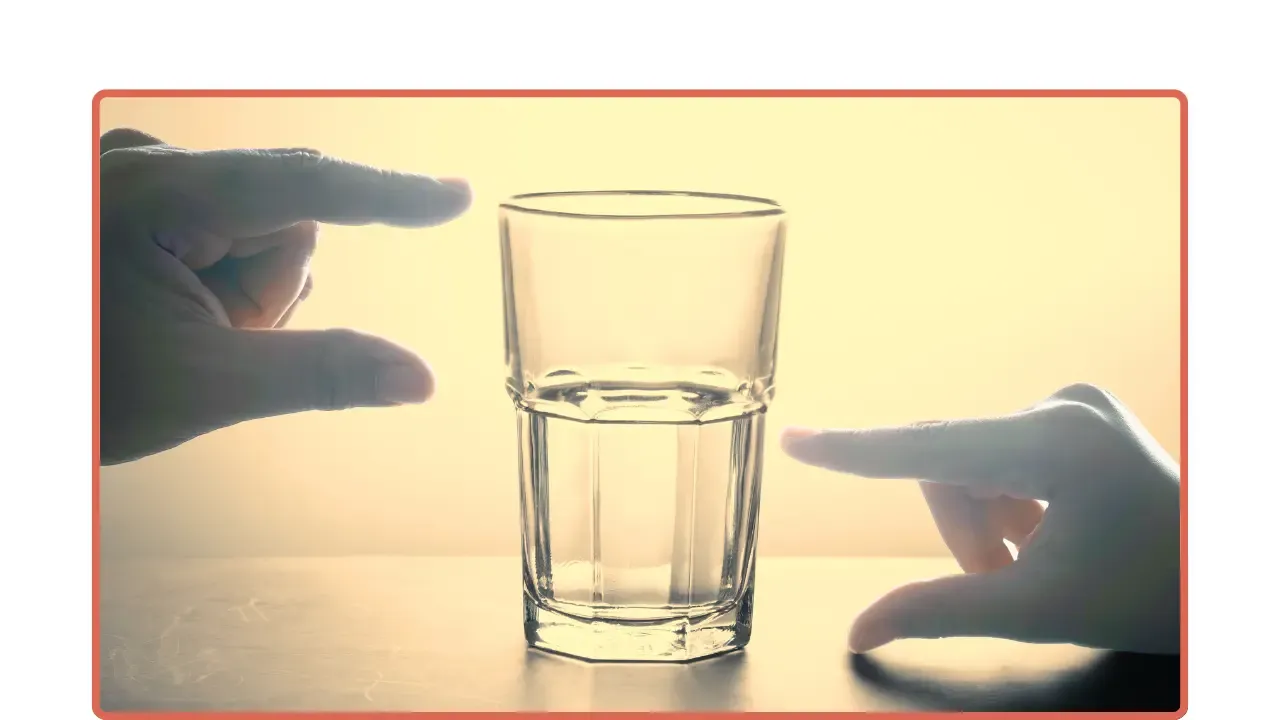 Un vaso con la mitad de agua y dos manos