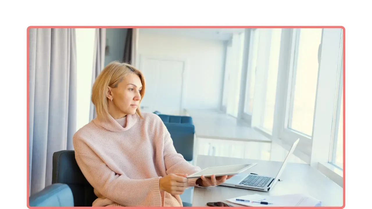 Mujer profesional sentada junto a una ventana, con una tablet y una laptop, reflexionando antes de iniciar un cambio profesional importante.