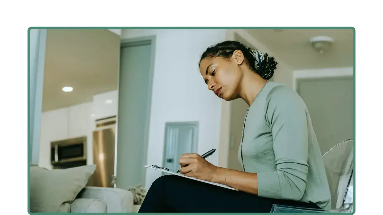 Mujer sentada escribiendo en una libreta en un espacio de trabajo en casa.