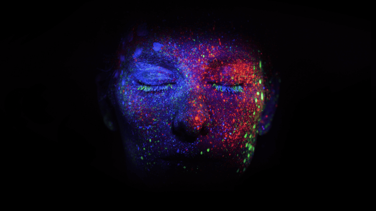 A face glows with dots of light, surrounded by darkness.