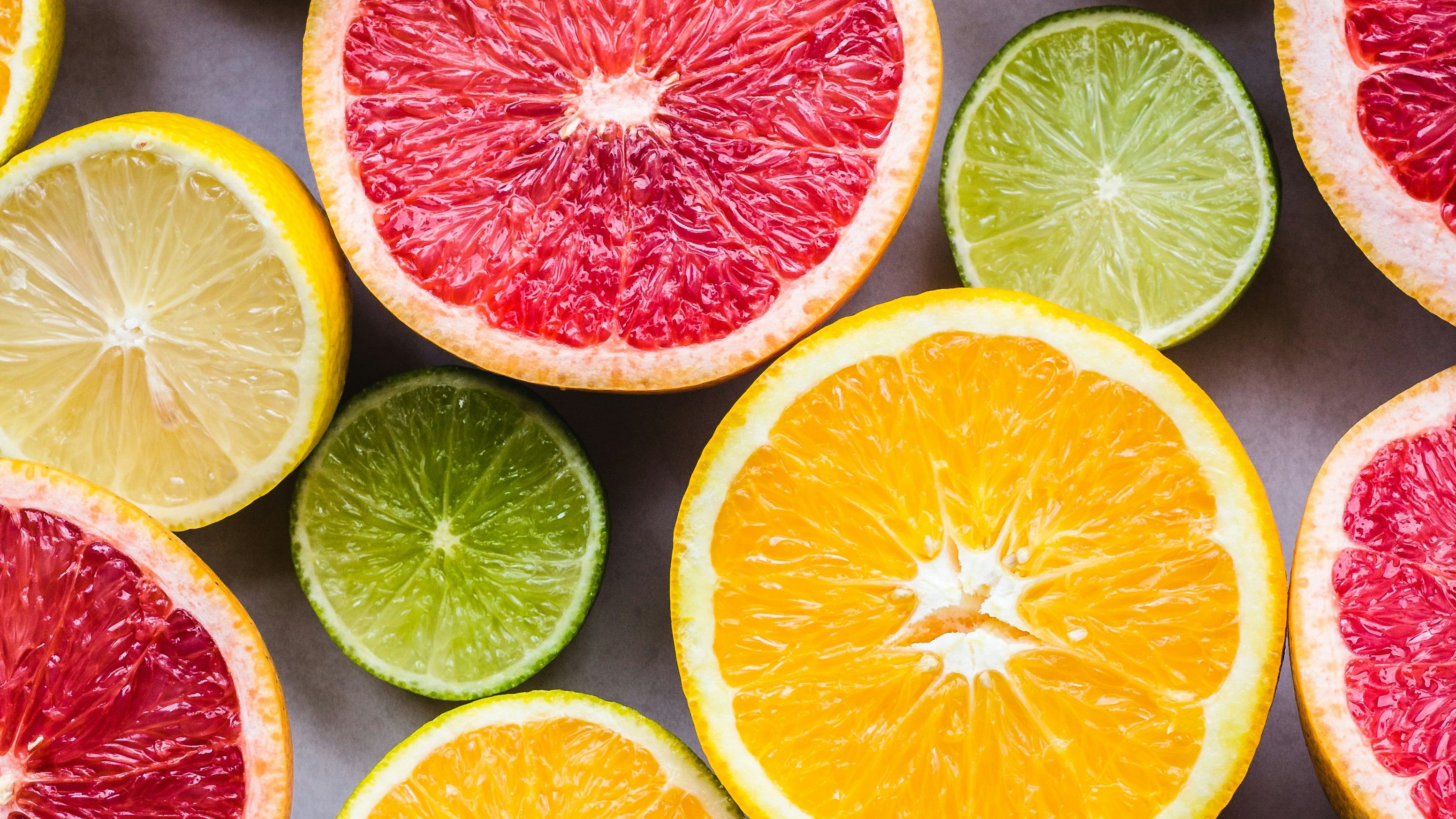 A vibrant, top-down arrangement of various citrus fruits sliced open—including oranges, grapefruits, lemons, and limes—revealing their juicy, colorful pulp and geometric patterns.