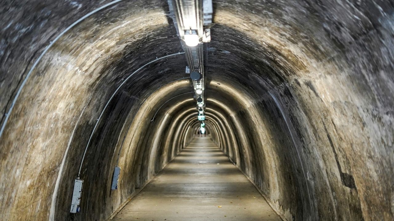 A dark underground tunnel, lights running at regular intervals along the ceiling, so light and dark patterns repeat along the tan walls of the tunnel.